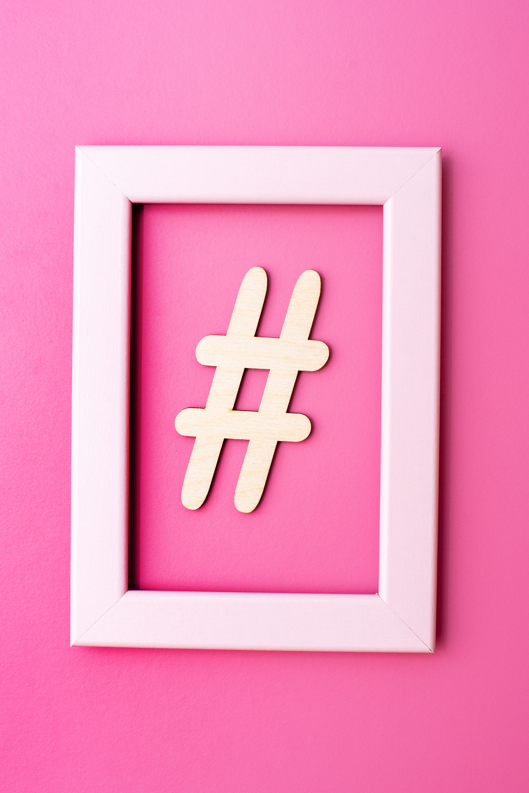 Hashtag sign made of wooden material in frame on pink background